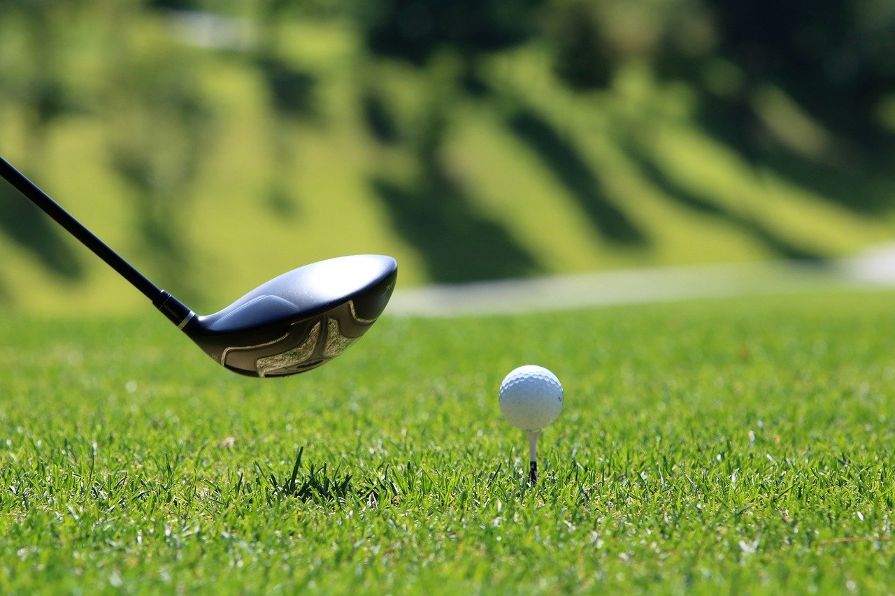 Man swinging a golf club on a green course, focused on his shot under clear skies.